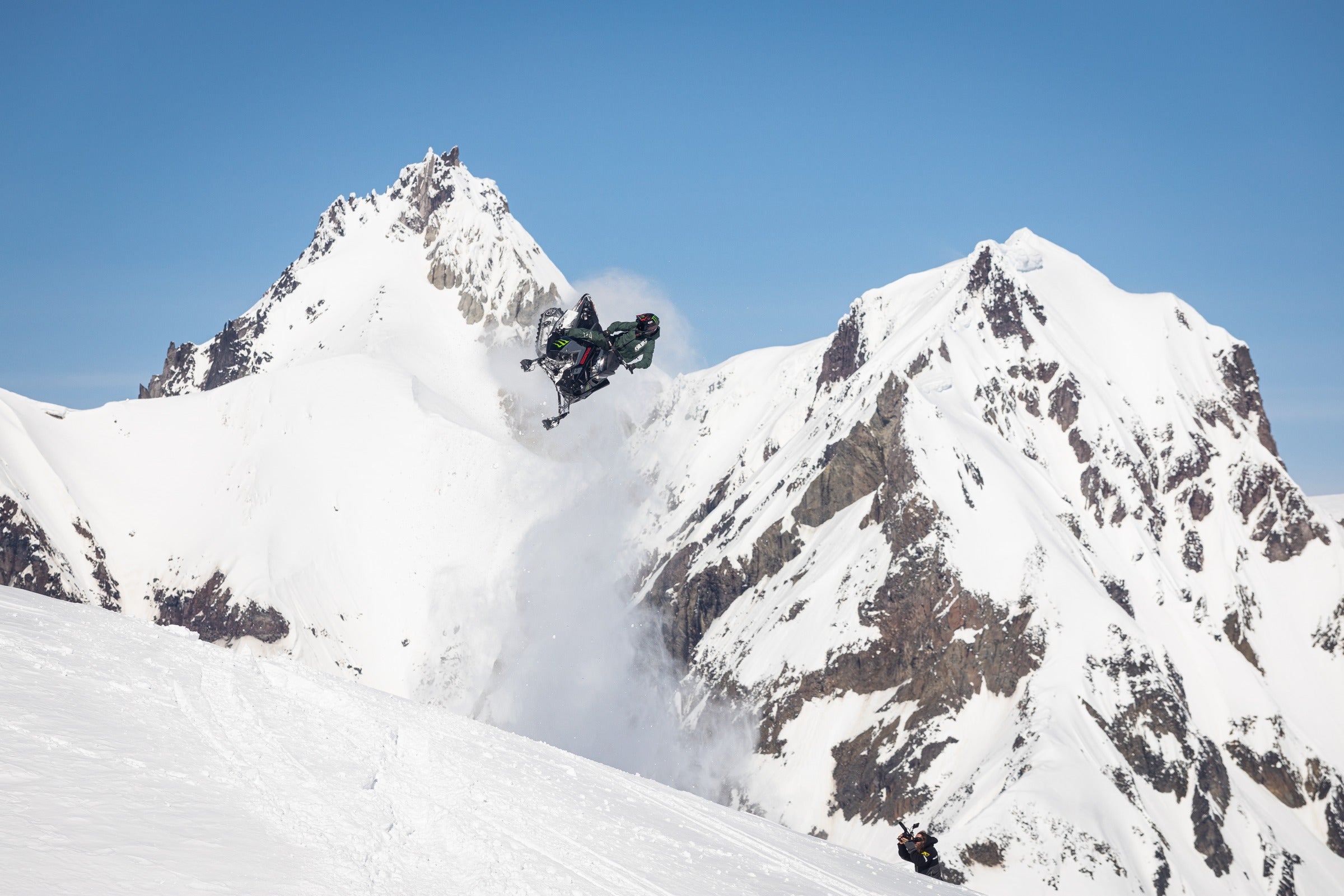 Airborne snowmobile rider framed by snow-covered alpine peaks